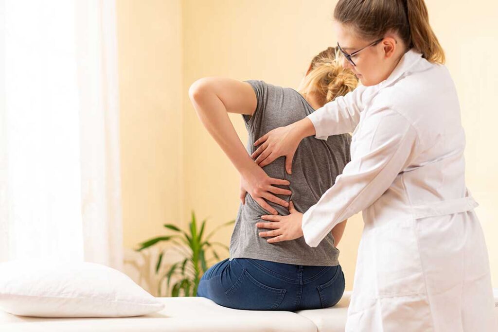 Person adjusting a monitor and keyboard at a home desk while stretching their shoulders.